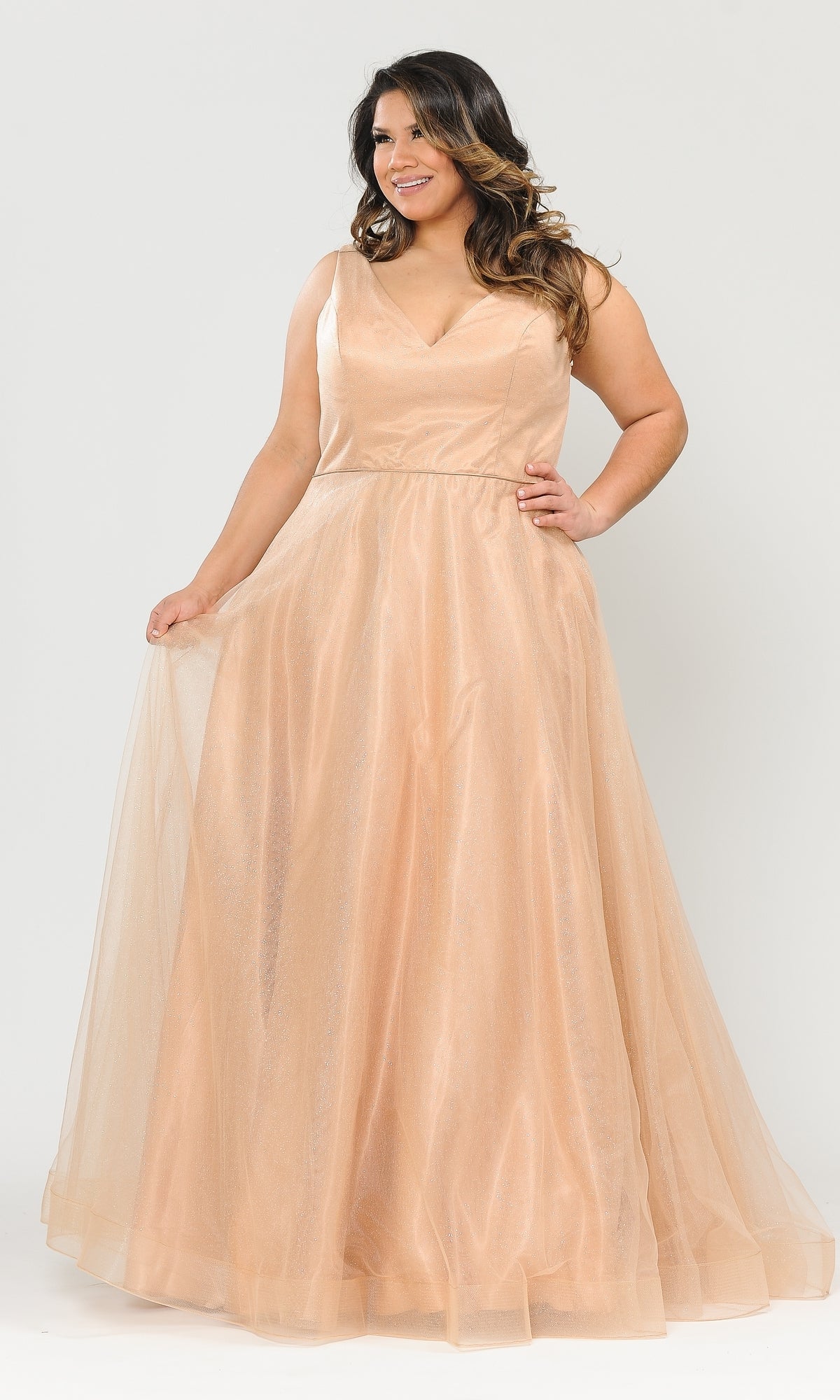 A woman wearing the Glitter-Tulle Plus-Size Long Prom Gown W1024, a peach-colored, sleeveless A-line dress with a V-neckline, stands against a white background, smiling and holding out her gown.